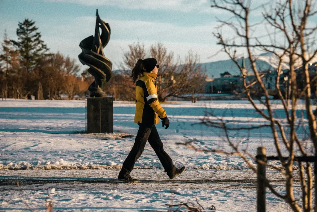 Femme qui marche dans la neige vétue d'une doudoune chauffante