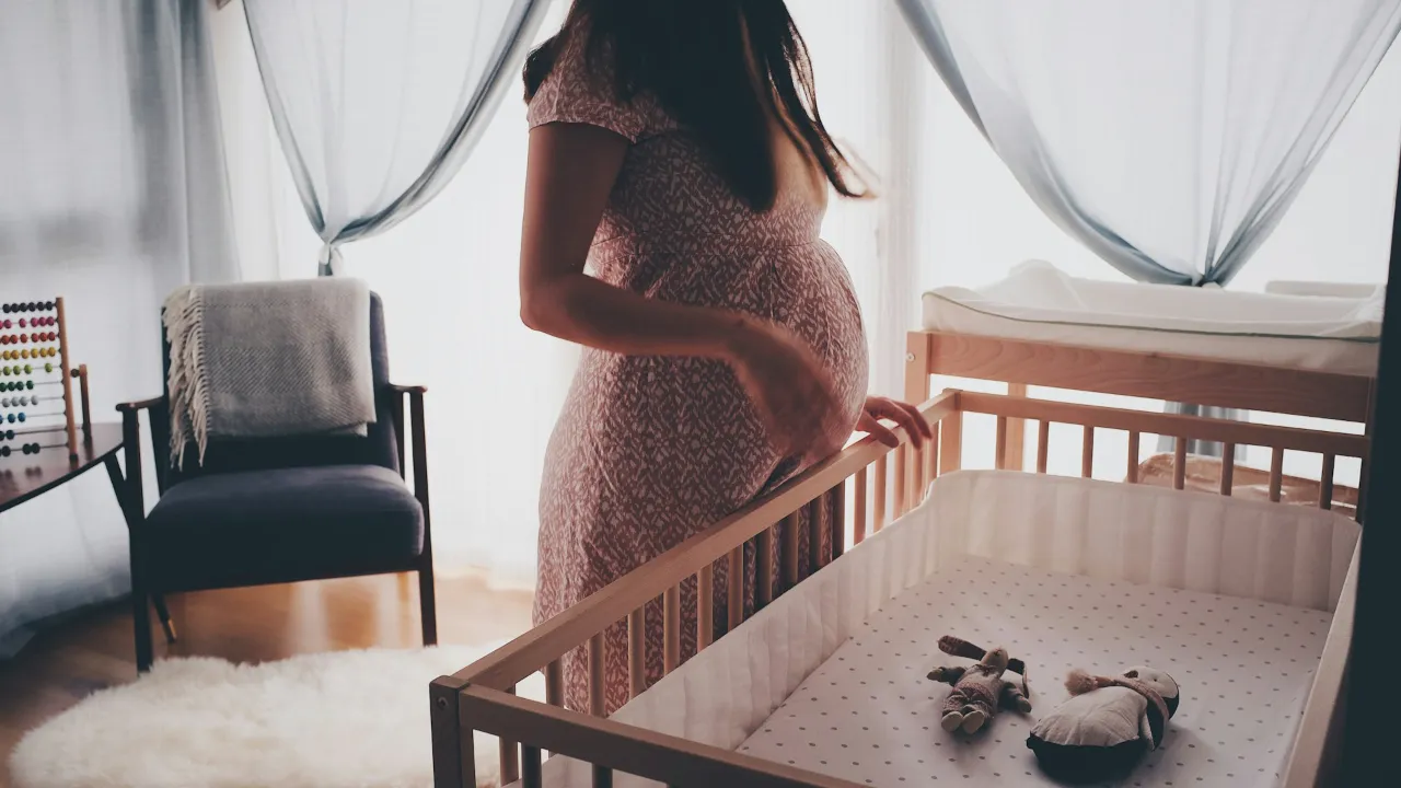Femme enceinte à côté d'un lit au design simple pour son futur bébé